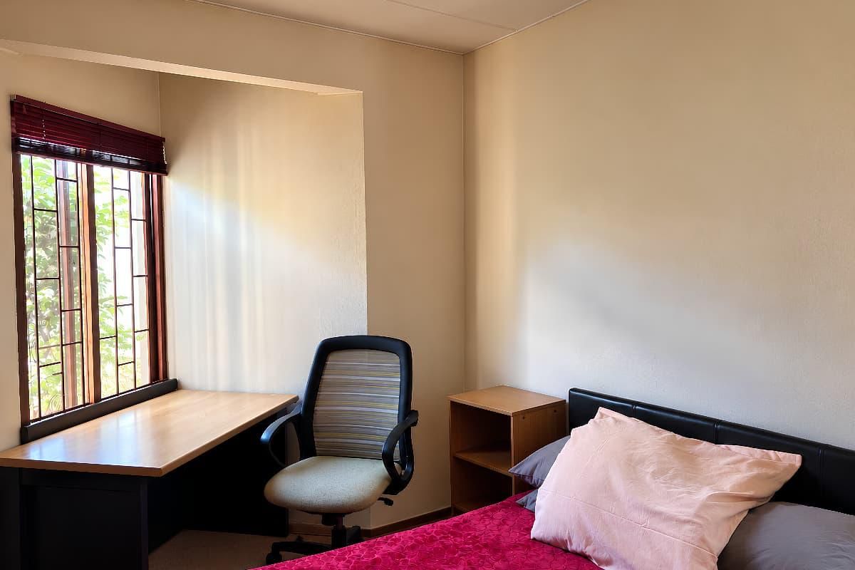 A functional bedroom featuring a built-in desk area, security bars on the window, and neutral wall finishes.