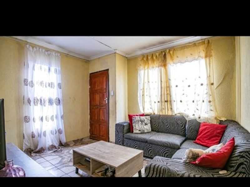 A living room area featuring tiled flooring and timber door access, currently showing signs of wear and requiring cosmetic updates to the walls and ceiling.