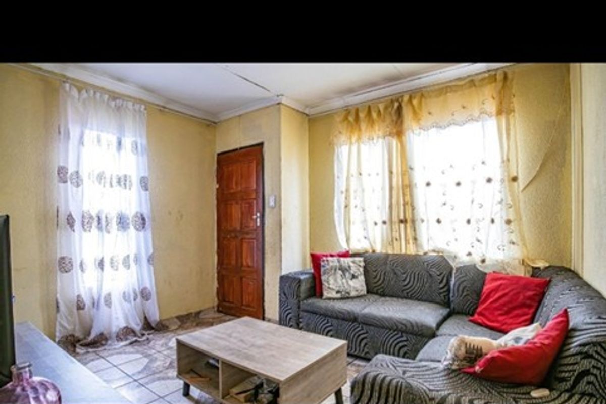 A living room area featuring tiled flooring and timber door access, currently showing signs of wear and requiring cosmetic updates to the walls and ceiling.