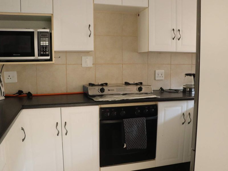 A functional kitchen featuring white cabinetry, dark countertops, tiled backsplash, and integrated cooking appliances including an oven and gas hob.