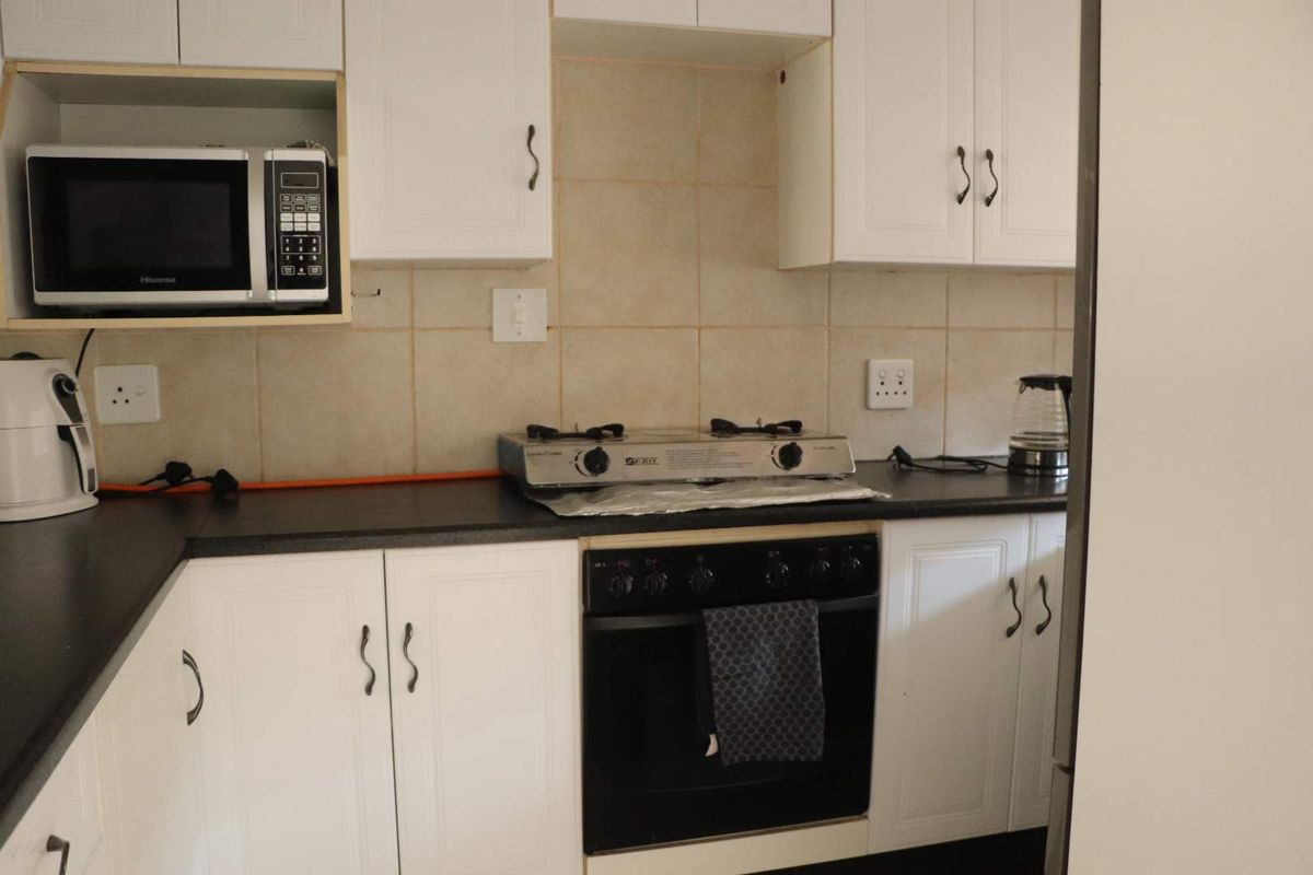 A functional kitchen featuring white cabinetry, dark countertops, tiled backsplash, and integrated cooking appliances including an oven and gas hob.