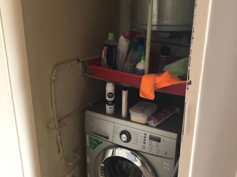 A compact laundry utility closet featuring a built-in electric water heater and plumbing connections for a washing machine.