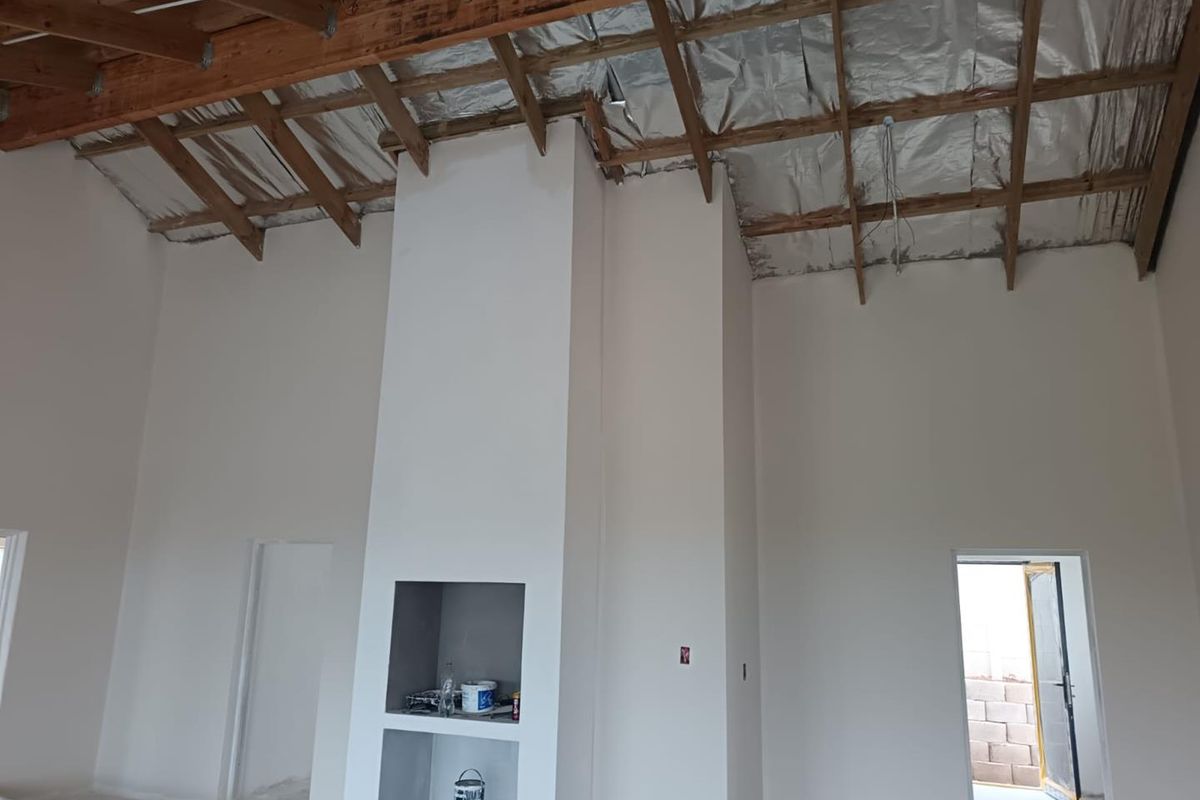 An unfinished living area featuring a central fireplace structure, exposed timber roof trusses, and reflective insulation, currently undergoing renovation.