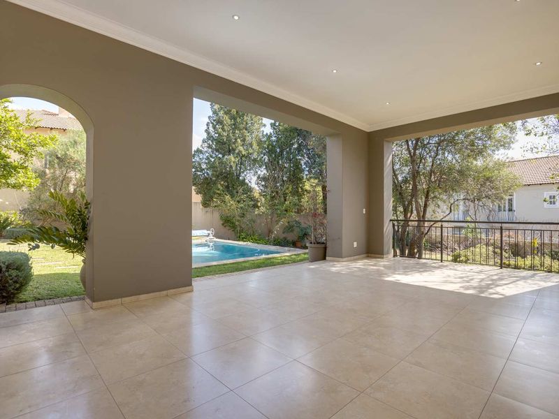 Spacious covered patio featuring tiled flooring, recessed lighting, and an arched transition to the garden and pool area.