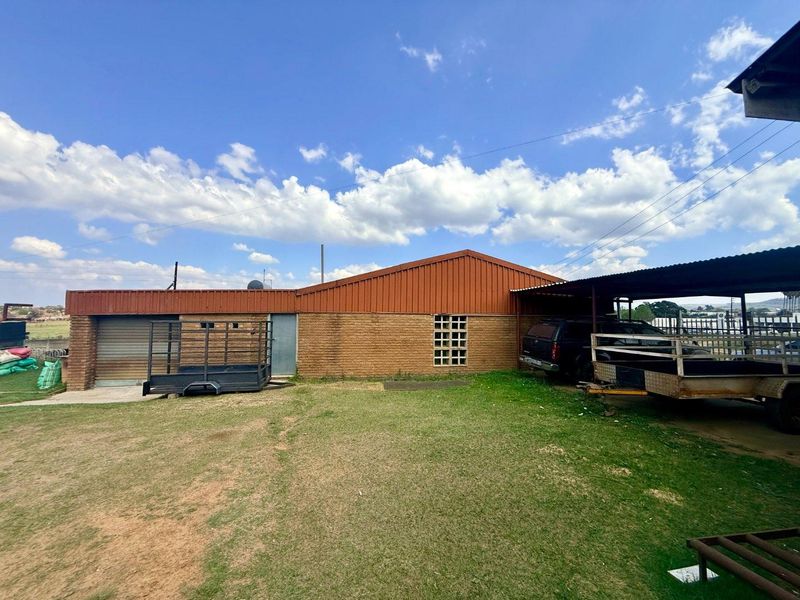 Rear exterior view of the office building featuring brick construction, a corrugated metal roof, a roller shutter door, and an attached carport structure.