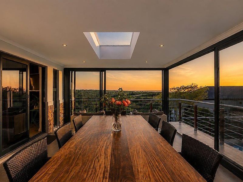 A modern covered balcony featuring a skylight, stone cladding, and expansive sliding glass doors offering panoramic sunset views.