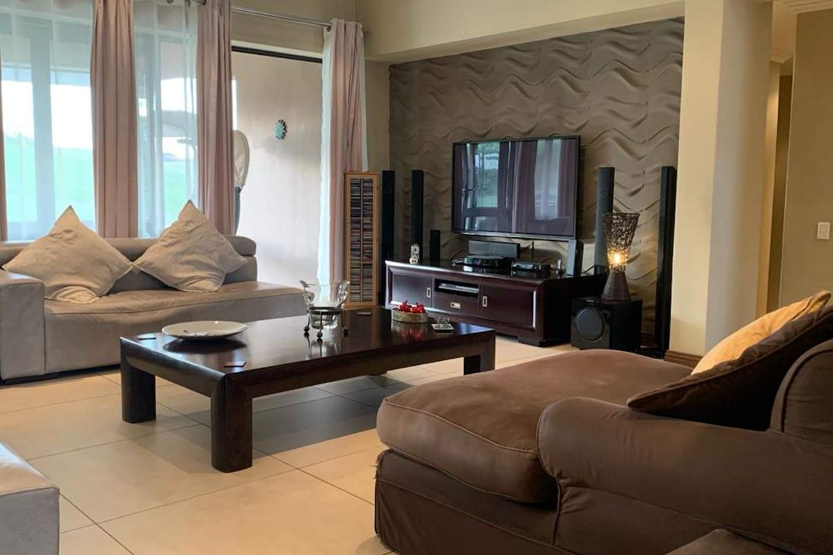 A comfortable living room featuring large format floor tiles and a textured feature wall, with direct access to an outdoor patio area.