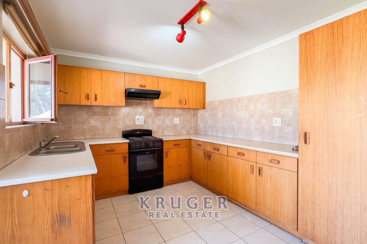 A functional kitchen featuring wooden cabinetry, laminate countertops, a freestanding stove with extractor fan, and tiled flooring throughout.