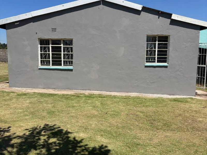 A view of the rear exterior facade featuring painted walls, steel-framed windows with security bars, and a surrounding lawn area.