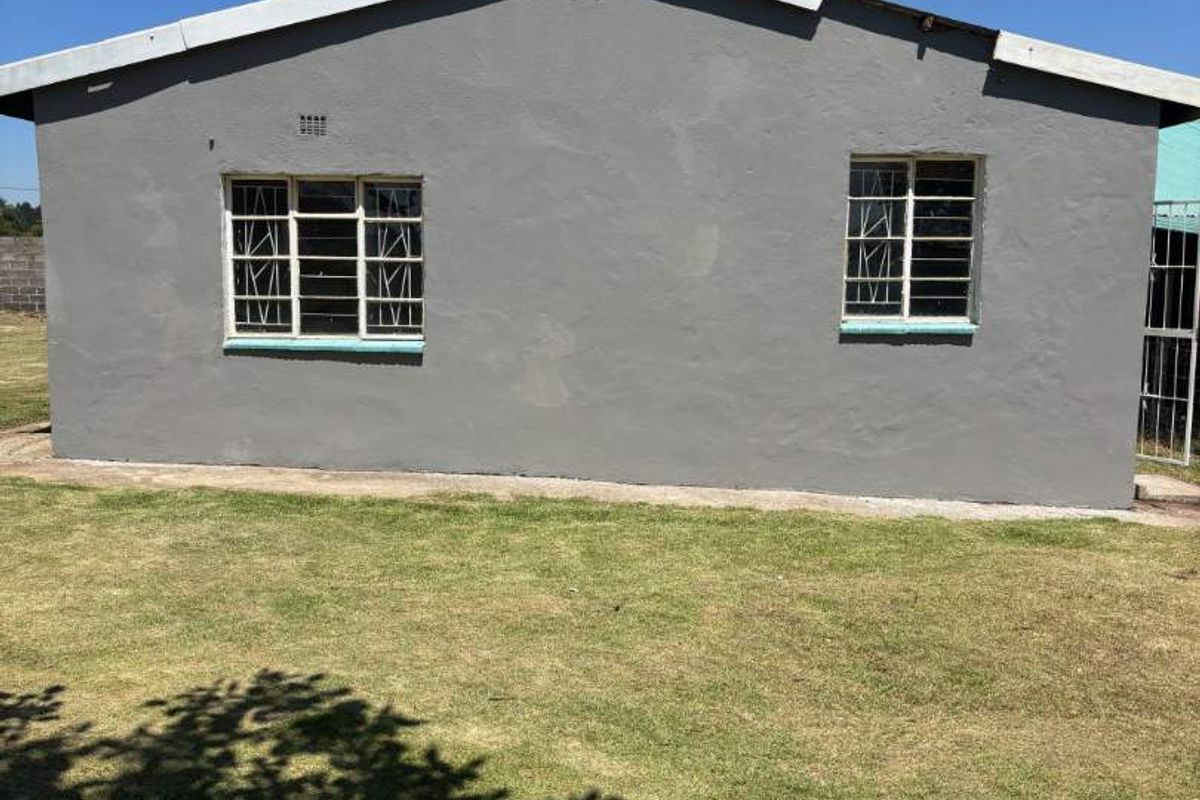 A view of the rear exterior facade featuring painted walls, steel-framed windows with security bars, and a surrounding lawn area.