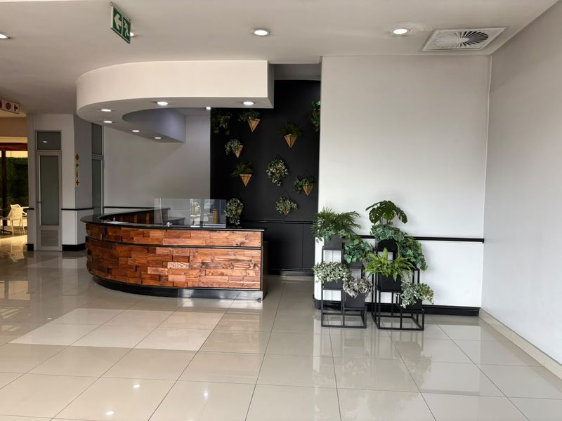 A modern office reception area featuring a curved wooden desk, tiled flooring, and recessed ceiling lighting in a professional commercial setting.