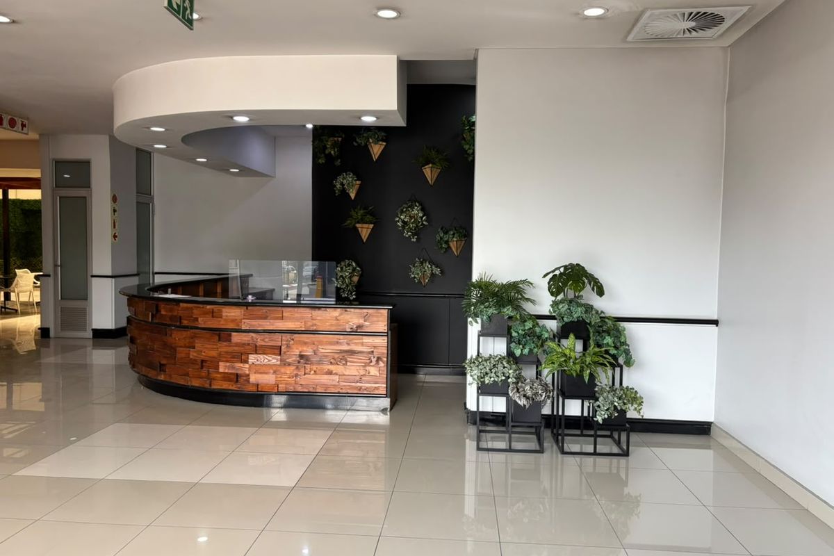 A modern office reception area featuring a curved wooden desk, tiled flooring, and recessed ceiling lighting in a professional commercial setting.