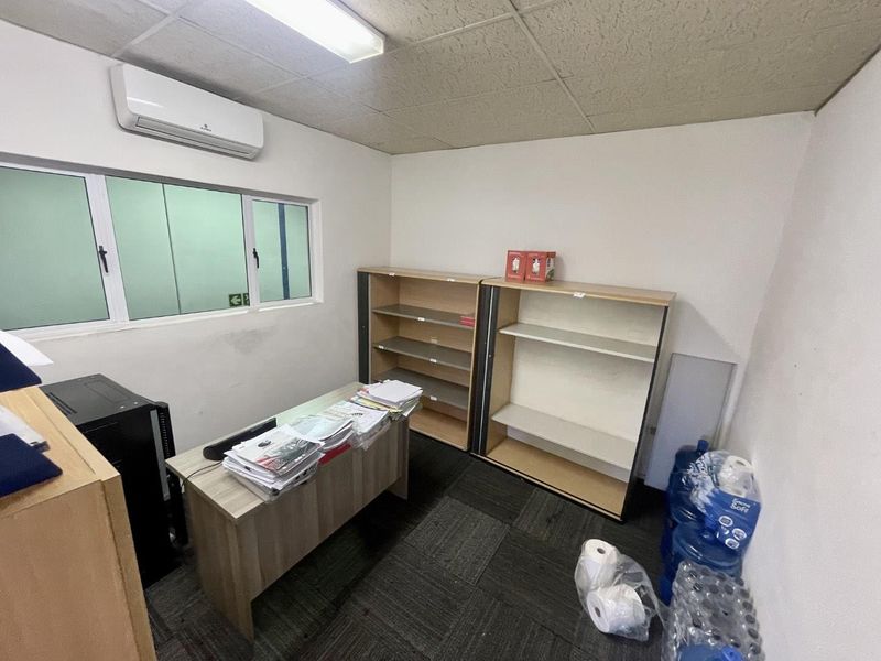 A functional office space featuring carpet tiles, a drop ceiling, and a wall-mounted air conditioning unit, suitable for a professional workspace.