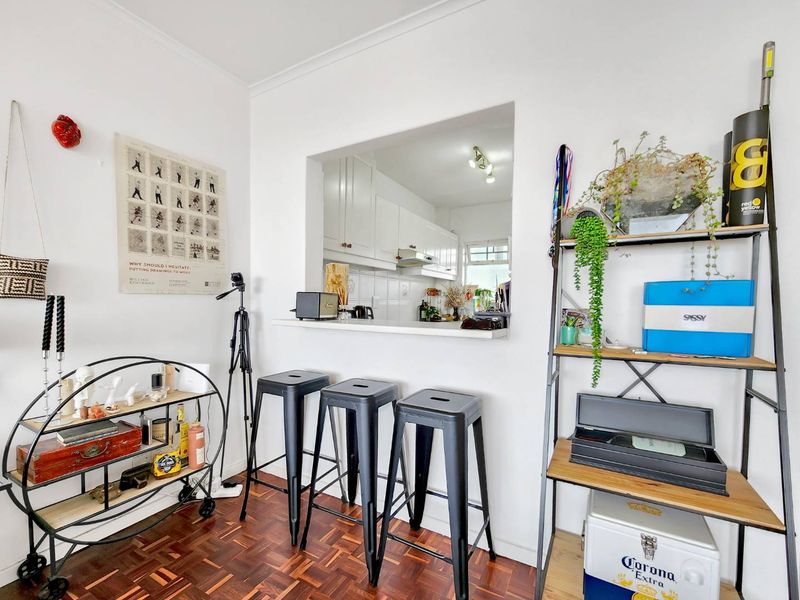 Open plan living area featuring a kitchen pass-through window, parquet flooring, and white cabinetry, creating a functional and connected space.