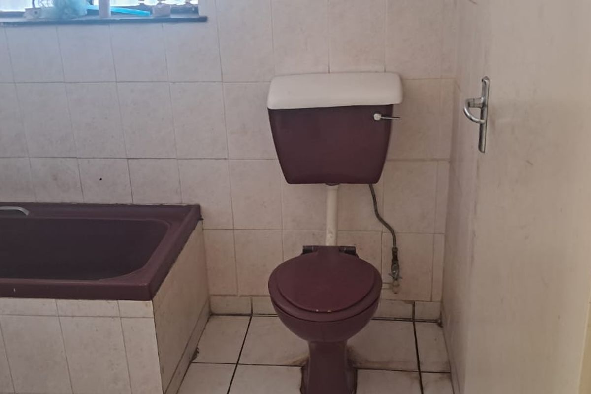A dated bathroom featuring a built-in bathtub and toilet with original colored sanitary ware and tiled wall finishes.