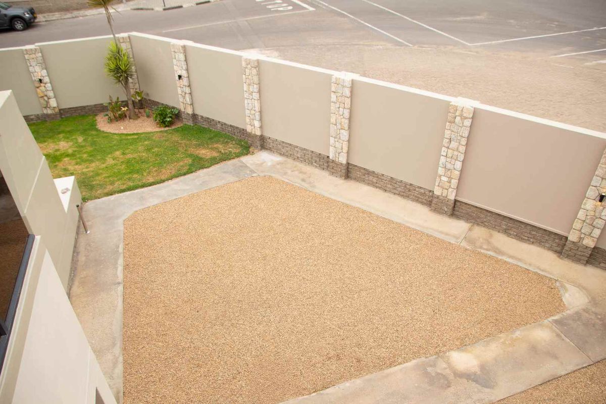 An elevated view of a low-maintenance rear courtyard featuring a gravel surface, a small lawn area, and a secure boundary wall with stone-clad pillars.