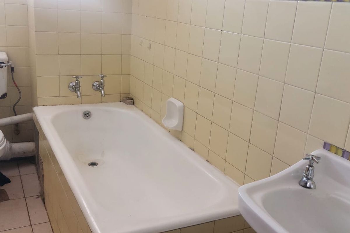 A dated bathroom featuring a standard bathtub, pedestal basin, and toilet with original yellow wall tiling and ceramic floor tiles.
