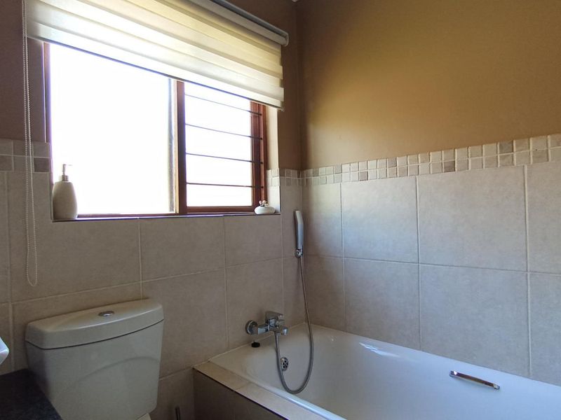 A functional bathroom featuring a bathtub with a handheld shower mixer, a toilet, and neutral wall tiling with a decorative border.