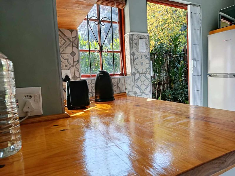 A cozy kitchen area featuring a polished timber countertop, decorative patterned tile splashback, and direct access to the garden through a side door.