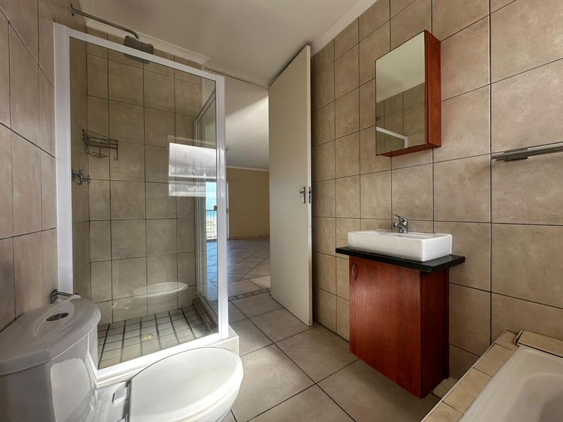 A functional bathroom featuring a glass shower enclosure, wall-mounted vanity with vessel sink, and neutral floor-to-ceiling tiling.