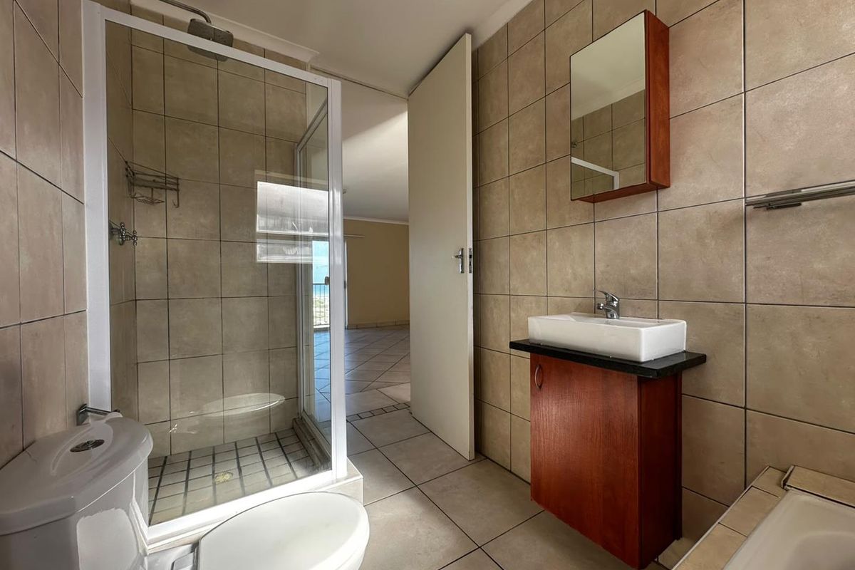 A functional bathroom featuring a glass shower enclosure, wall-mounted vanity with vessel sink, and neutral floor-to-ceiling tiling.