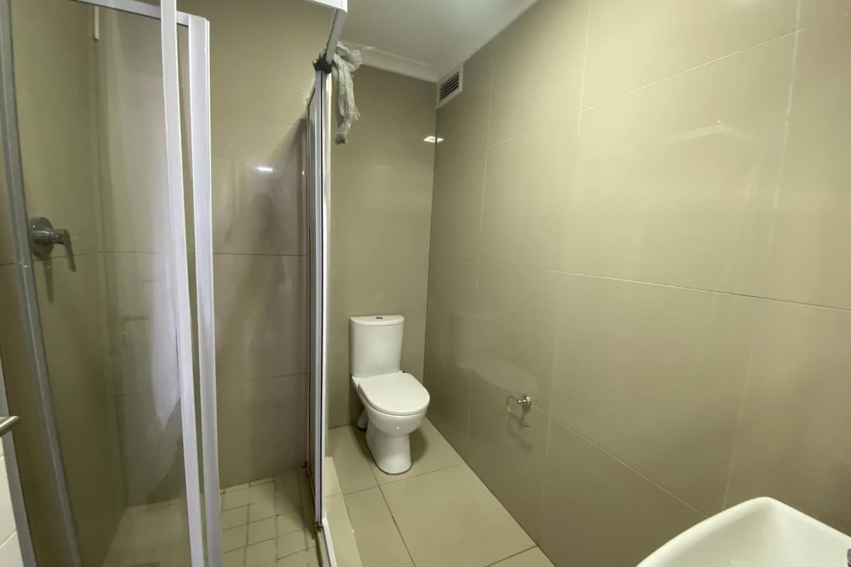 A functional bathroom featuring a glass-enclosed shower, a standard toilet, and neutral wall tiling throughout.