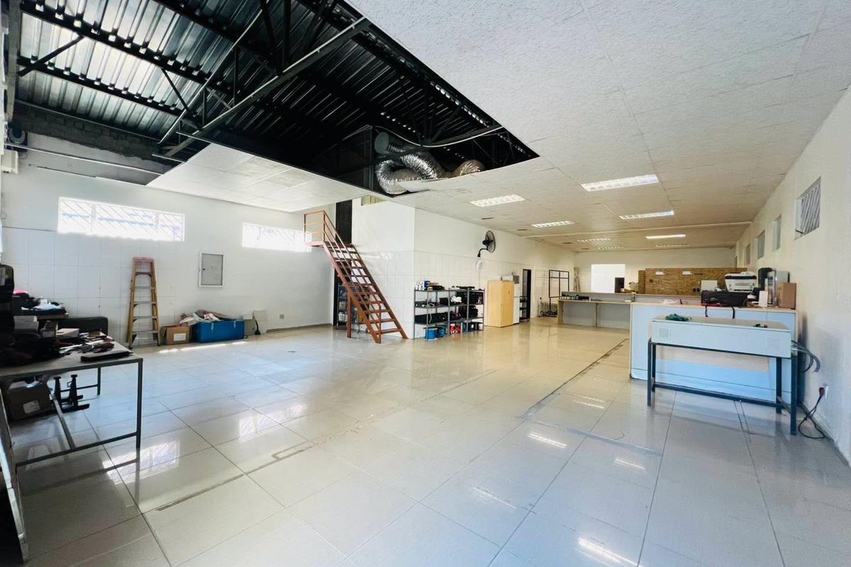 Spacious industrial utility area featuring tiled flooring, exposed ceiling structure with ventilation, and a mezzanine staircase, suitable for various commercial or workshop applications.
