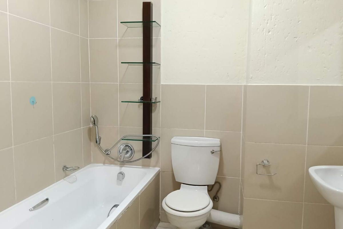 A functional bathroom featuring a bathtub, pedestal basin, and toilet with neutral wall tiling and built-in glass shelving.