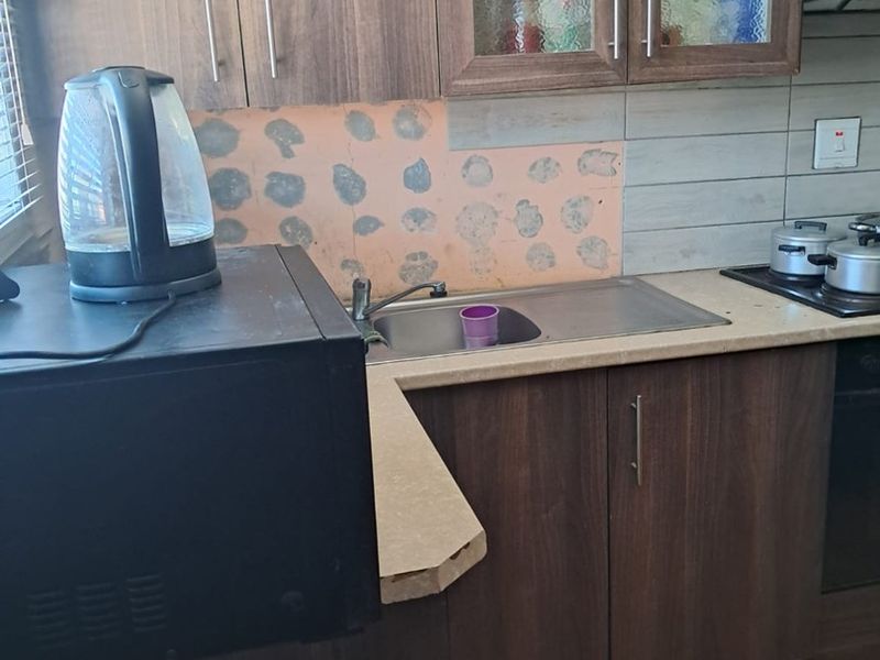 A functional kitchen featuring dark wood-look cabinetry, a stainless steel sink, and built-in cooking appliances, requiring minor cosmetic repairs to the splashback area.