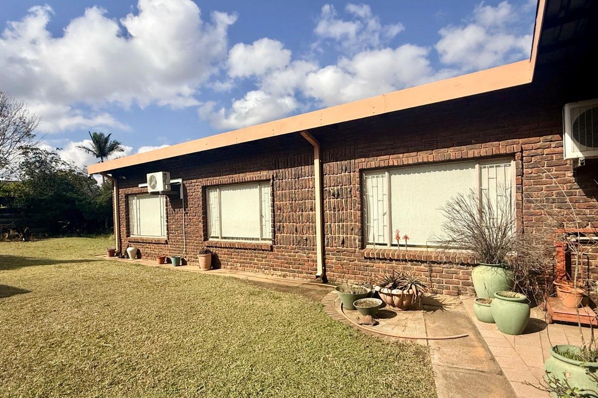 A view of the rear exterior of the house featuring face-brick walls, large windows with security bars, and an adjacent lawn area.