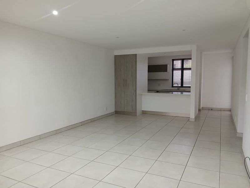 Spacious open-plan living area featuring neutral tiled flooring, recessed lighting, and a functional kitchen pass-through with built-in cabinetry.