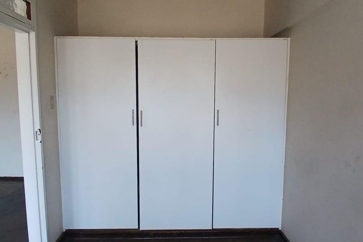 A bedroom featuring a built-in white wardrobe with clean lines, offering practical storage space in a neutral setting.