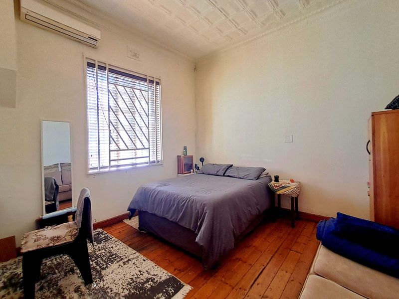 A bedroom featuring original timber flooring, a decorative pressed metal ceiling, and a wall-mounted split system air conditioner.