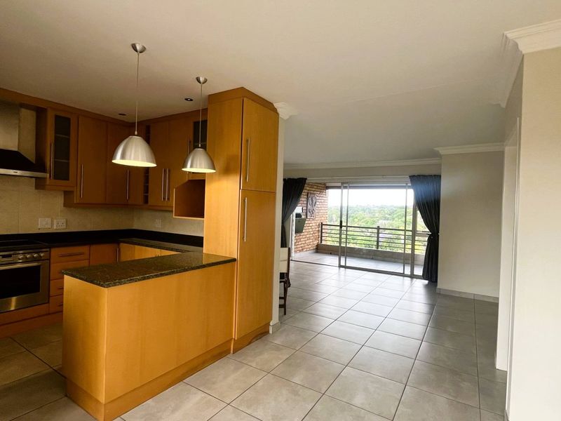 Open-plan kitchen and living area featuring wooden cabinetry, granite countertops, and direct access to a balcony with scenic views.