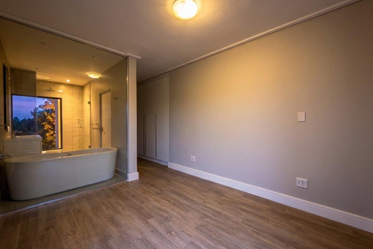 A spacious bedroom featuring modern laminate flooring, built-in cupboards, and an open-plan en-suite bathroom with a freestanding bathtub and glass partition.