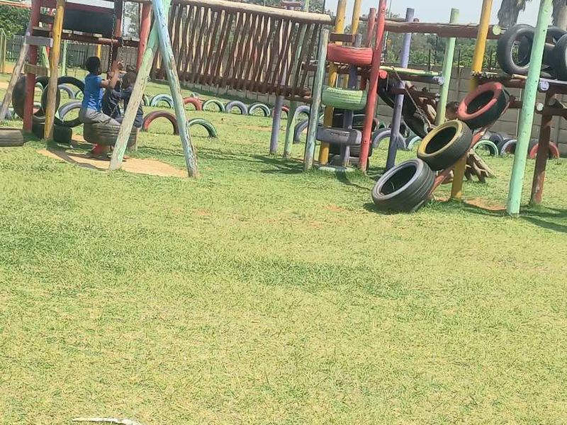 Outdoor communal playground area featuring timber climbing frames and swing sets situated on a grass lawn.