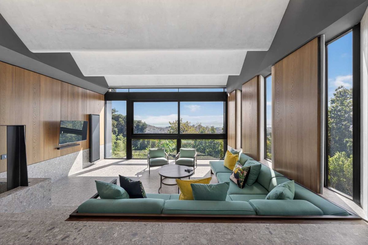 Modern sunken living room featuring high-end timber wall paneling, stone flooring, and expansive windows offering panoramic views.