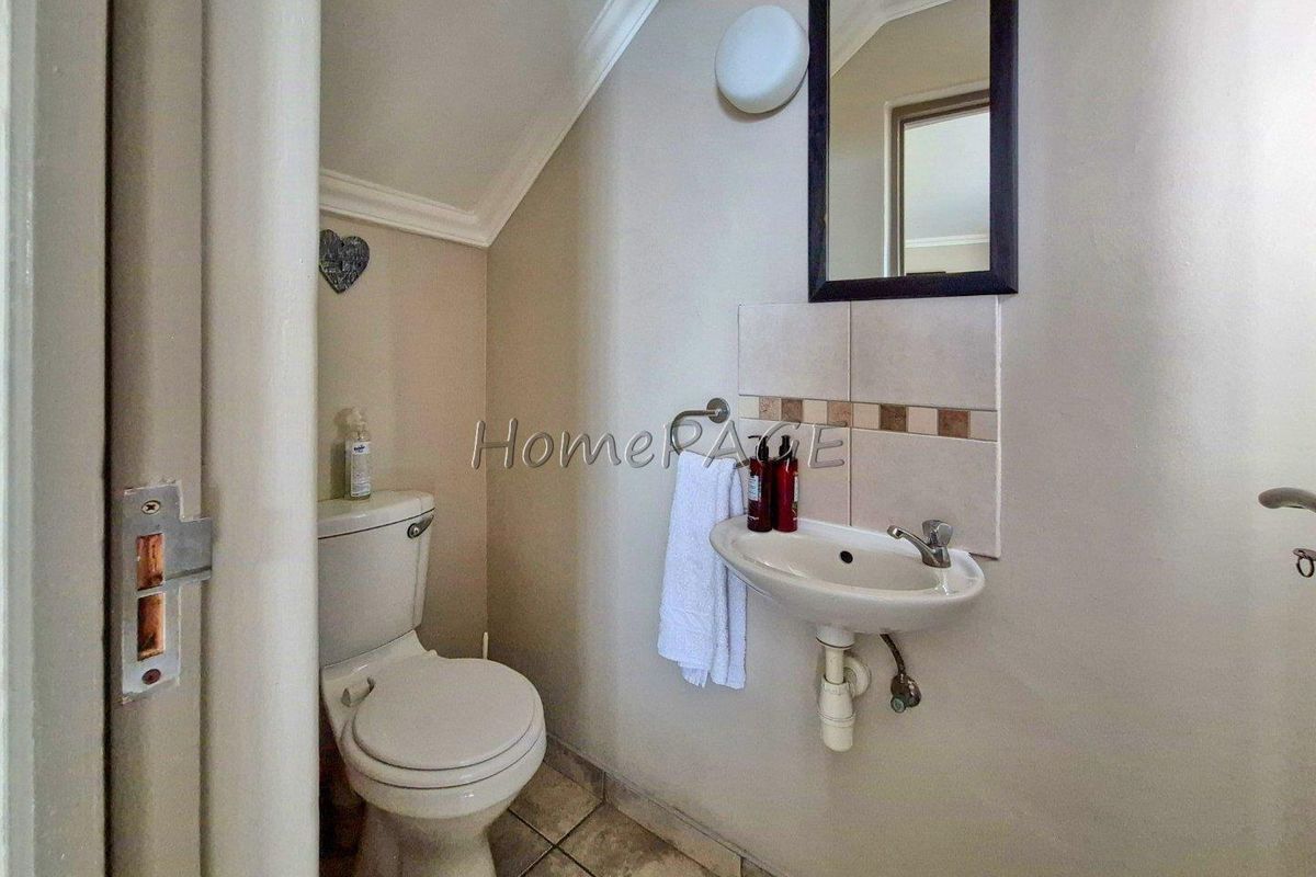 A compact guest cloakroom featuring a wall-mounted basin, toilet, and tiled flooring, situated under a sloped ceiling.