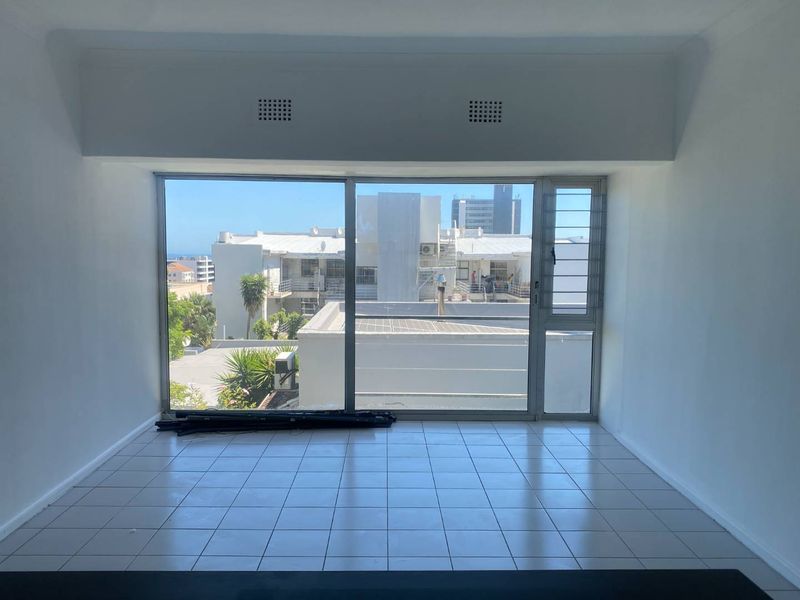 An empty, sunlit living area featuring large sliding glass doors that provide ample natural light and an urban view.