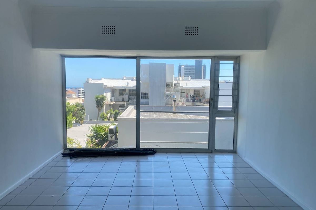An empty, sunlit living area featuring large sliding glass doors that provide ample natural light and an urban view.