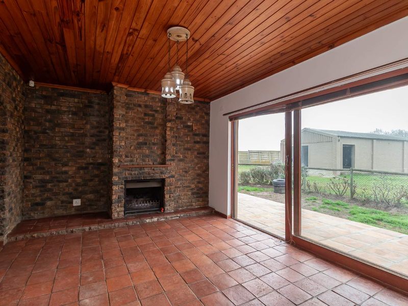 Spacious living room featuring a rustic exposed brick fireplace, timber ceiling, terracotta flooring, and large sliding doors opening to the garden.