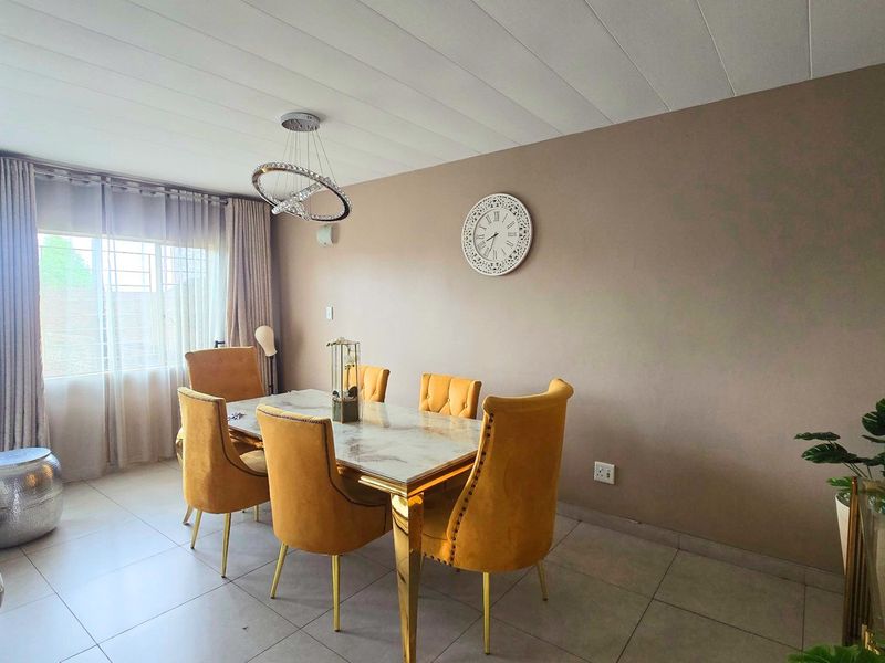 A well-lit dining area featuring tiled flooring, a modern pendant light fixture, and large windows with security bars.