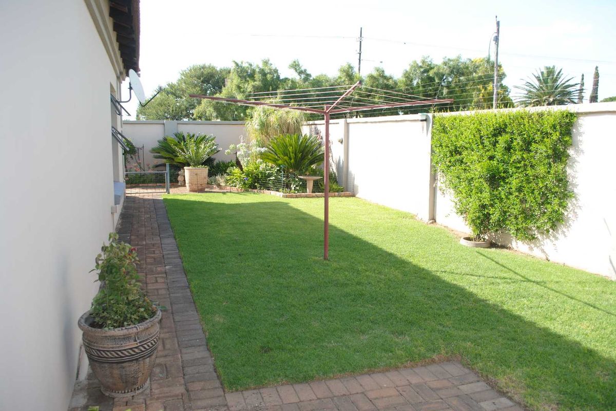A private rear garden featuring a well-maintained lawn, paved walkway, and perimeter boundary walls.