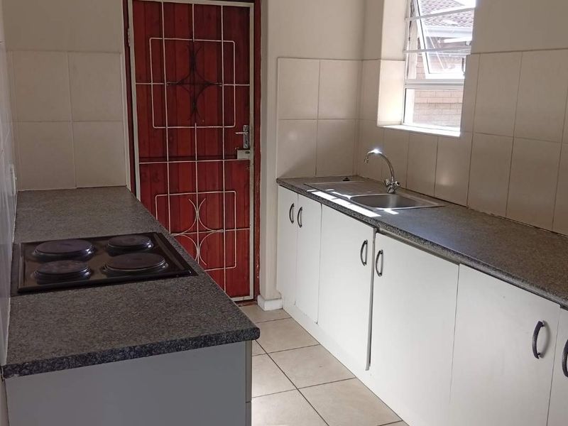 A functional kitchen featuring white built-in cabinetry, laminate countertops, a stainless steel sink, and an electric hob with tiled flooring and backsplash.