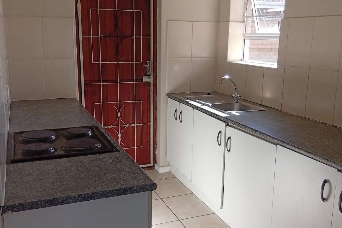 A functional kitchen featuring white built-in cabinetry, laminate countertops, a stainless steel sink, and an electric hob with tiled flooring and backsplash.