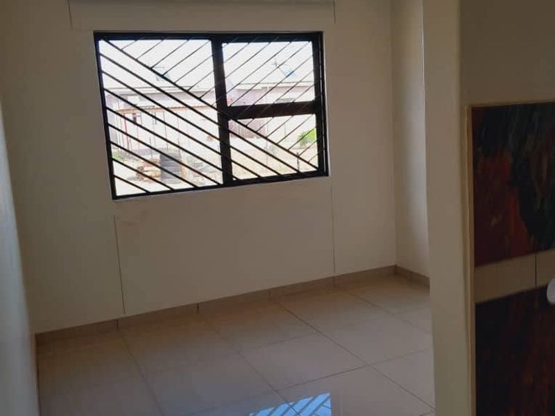 A clean, empty bedroom featuring neutral tiled flooring, a window with security bars, and a simple ceiling light fixture.