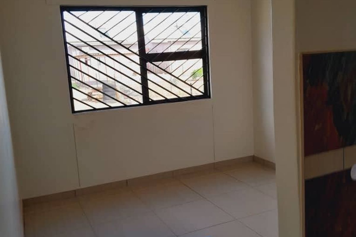 A clean, empty bedroom featuring neutral tiled flooring, a window with security bars, and a simple ceiling light fixture.