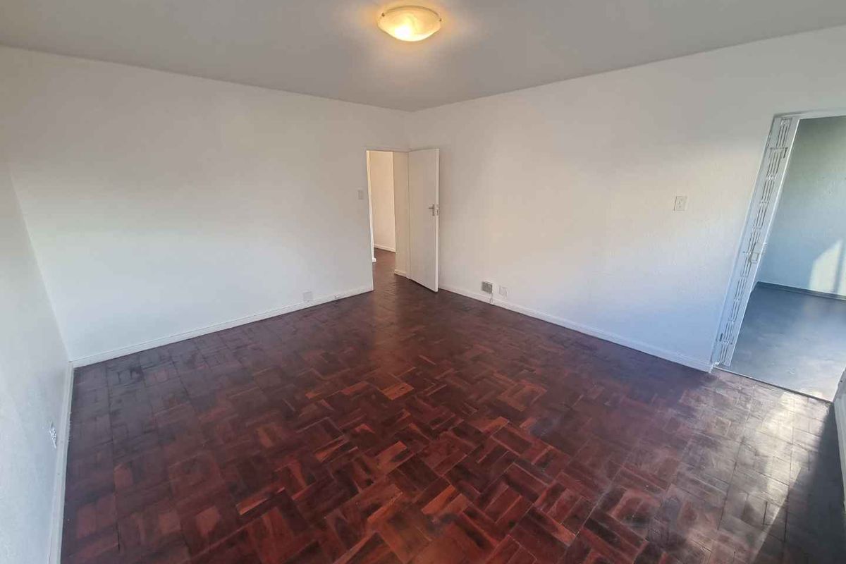 A spacious, empty living room featuring traditional parquet wood flooring and neutral white walls, providing a versatile blank canvas for interior design.