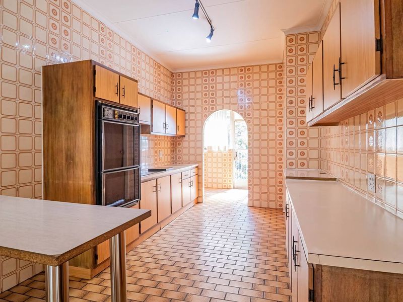 A spacious, dated kitchen featuring extensive wall tiling, built-in double oven, and ample cabinetry, offering significant potential for a modern renovation.