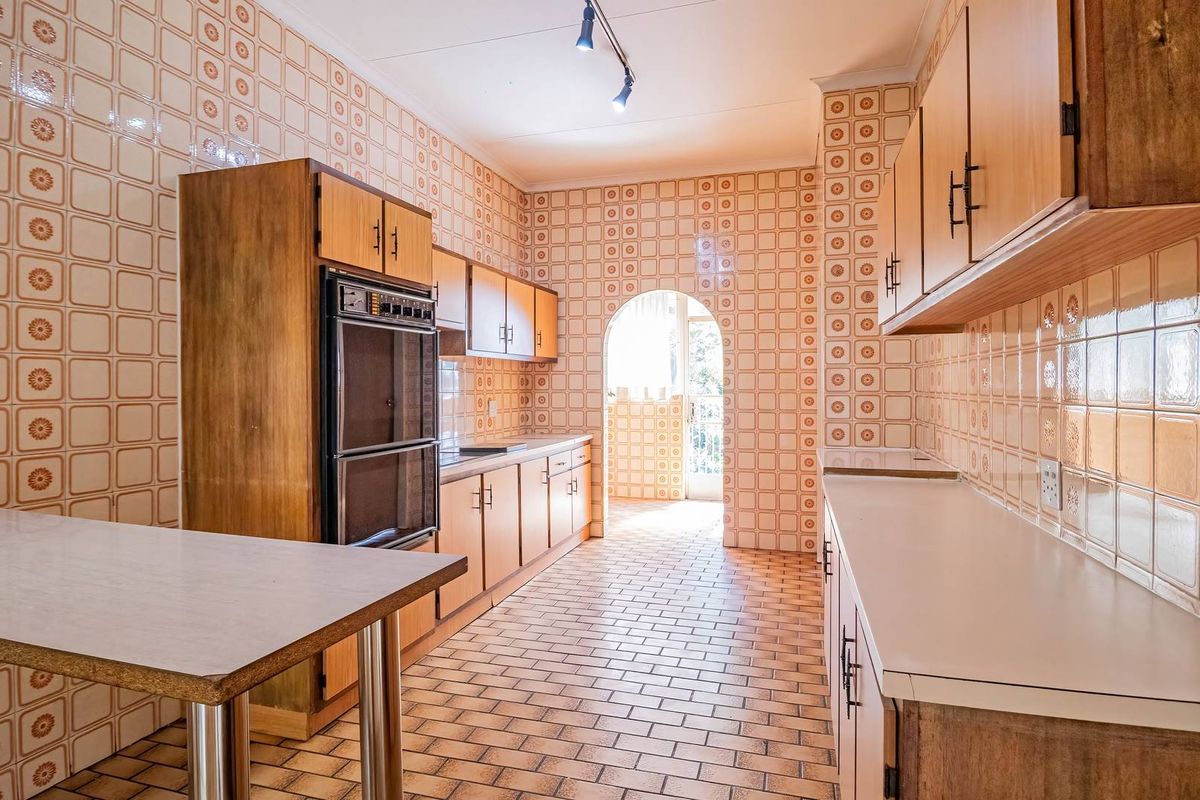 A spacious, dated kitchen featuring extensive wall tiling, built-in double oven, and ample cabinetry, offering significant potential for a modern renovation.